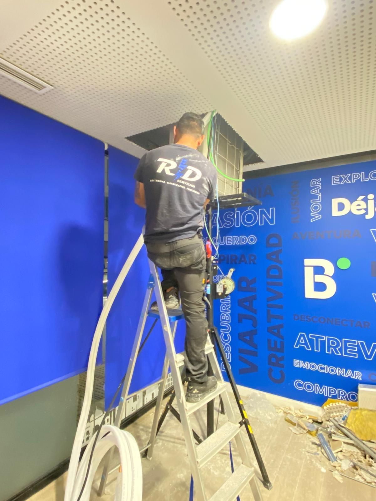 Un trabajador subido a una escalera instala un letrero en una pared azul dentro de una habitación luminosa.