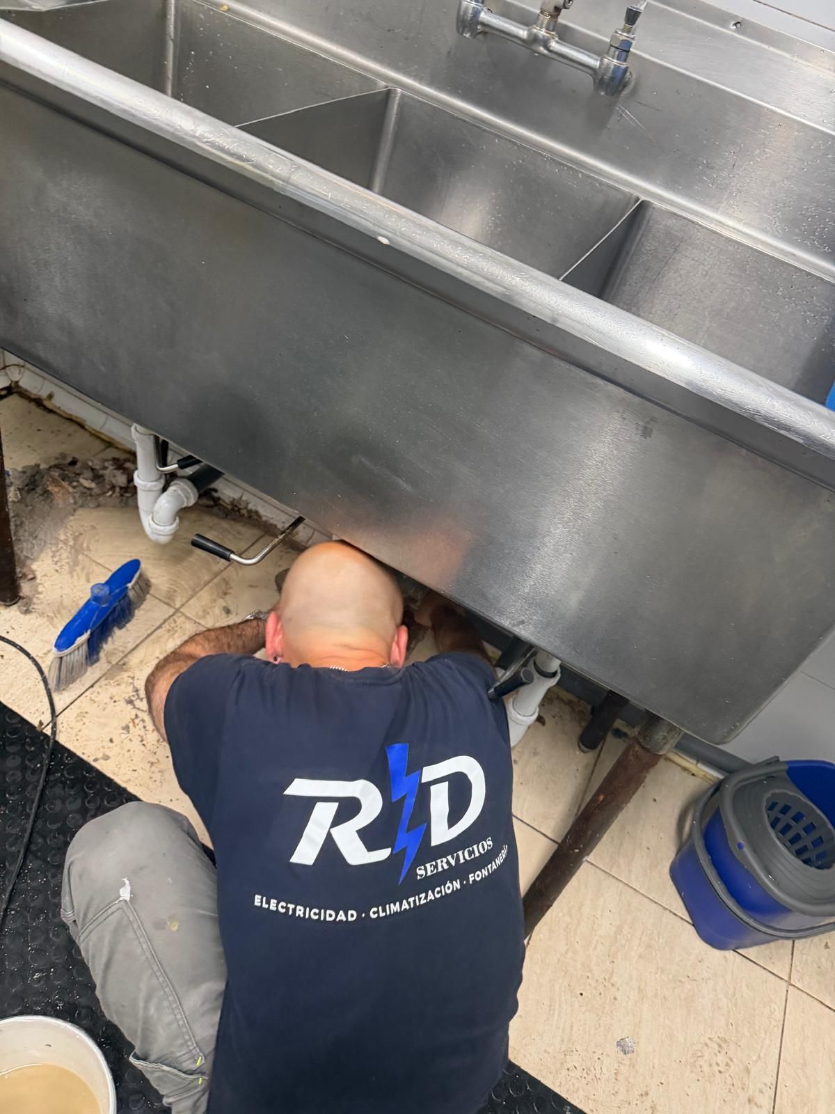 Fontanero trabajando debajo de un fregadero de acero inoxidable con herramientas