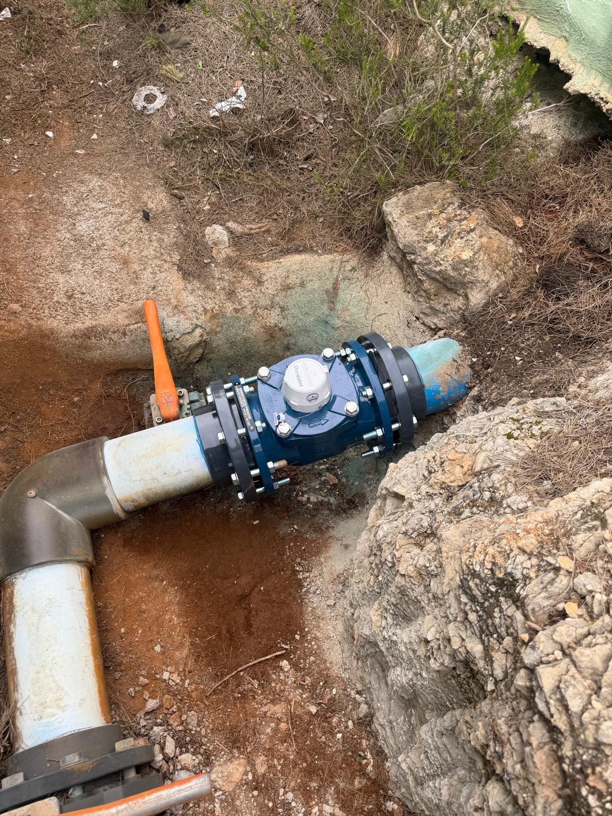 Conexión de tubería subterránea azul con válvula junto a rocas y tierra en una obra de construcción.