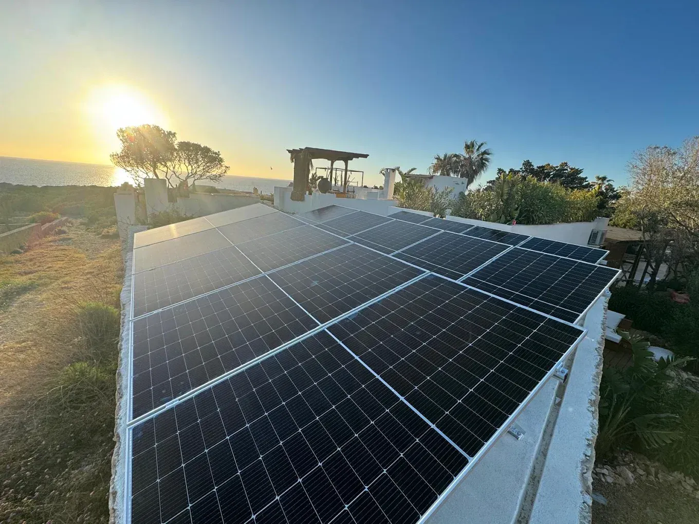 Paneles solares en una azotea al atardecer, con árboles y un cielo azul despejado.