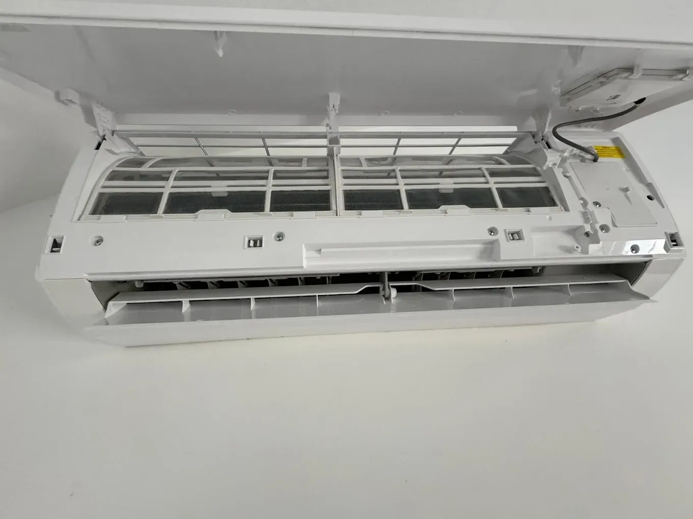 Aire acondicionado blanco de pared con el panel frontal abierto, dejando ver los filtros