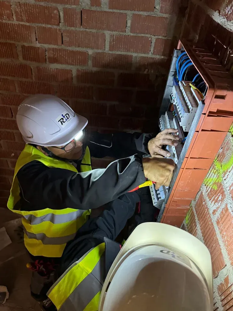 Electricista trabajando en el cableado expuesto en un cuarto de servicio de ladrillo cerca de un inodoro.
