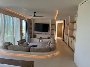 Sala de estar moderna con sofá curvo de color beige, televisor montado en la pared, estanterías de madera