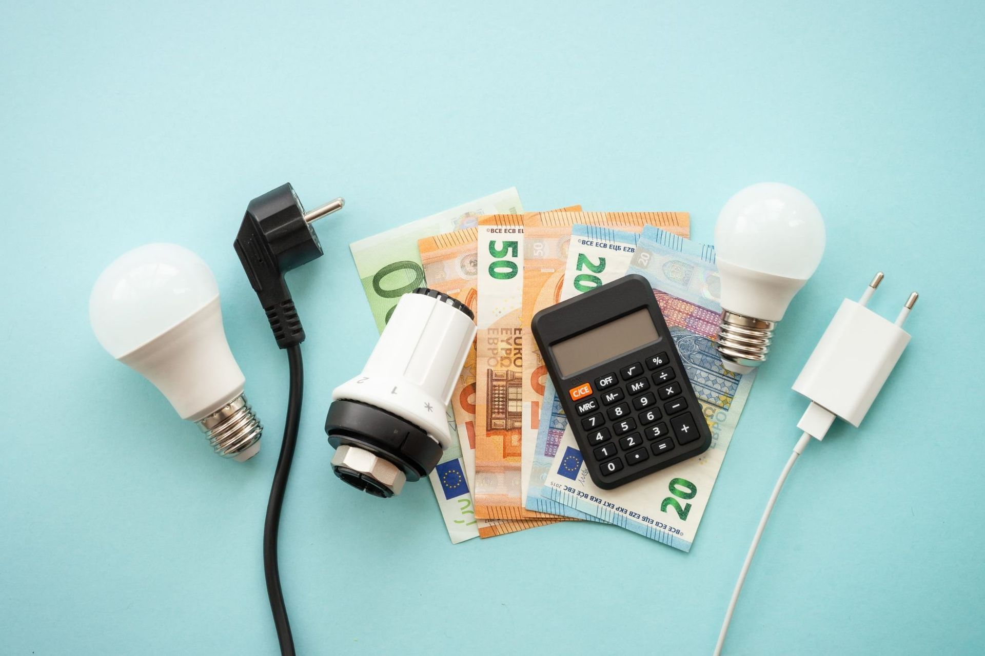 Bombillas, enchufes eléctricos y una calculadora en billetes de euro sobre un fondo azul.