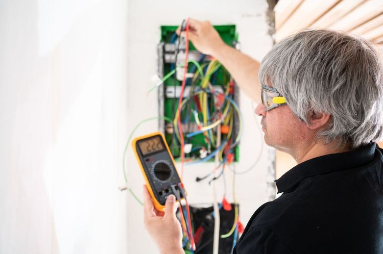 Técnico probando el cableado eléctrico expuesto con un multímetro en un panel de pared.