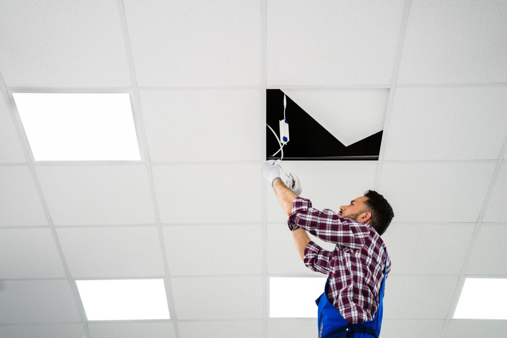 Técnico reparando un panel de techo en una oficina con falso techo.