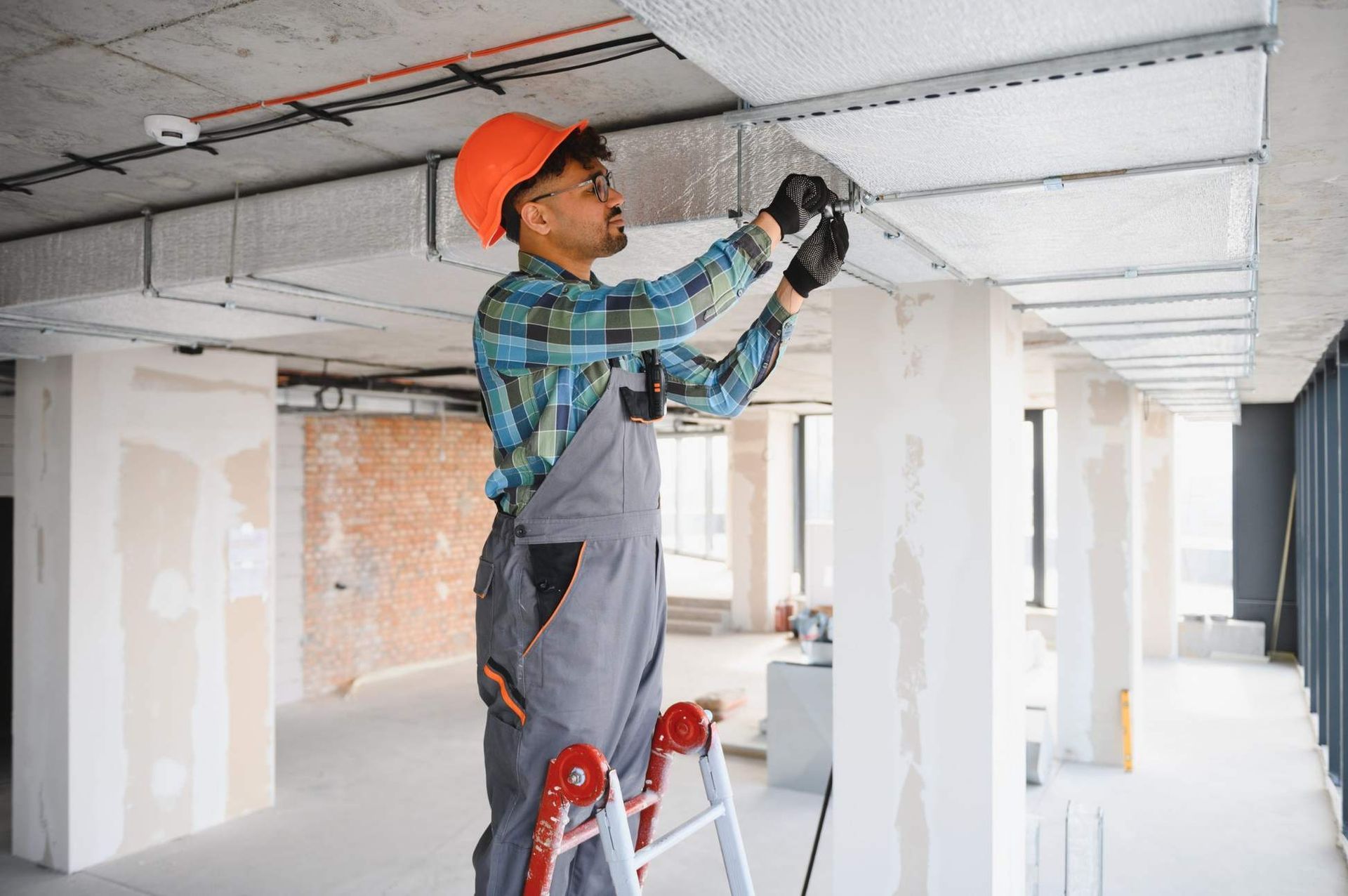 Obrero con casco naranja instalando un panel de techo en una obra de construcción.