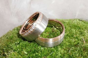 zwei zweifarbige Trauringe auf Moosfläche, einer davon mit Diamantenband