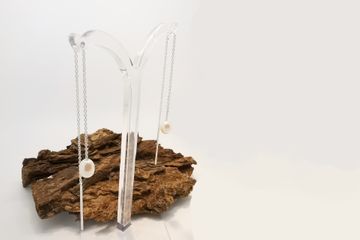 Schmuckhalter mit Fundament aus Holz, an dem zwei lange Ohrringe mit Perlen hängen