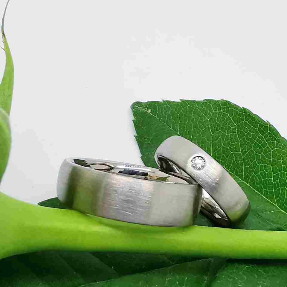 zwei Trauringe auf einer Blume, einer der Ringe hat einen Stein