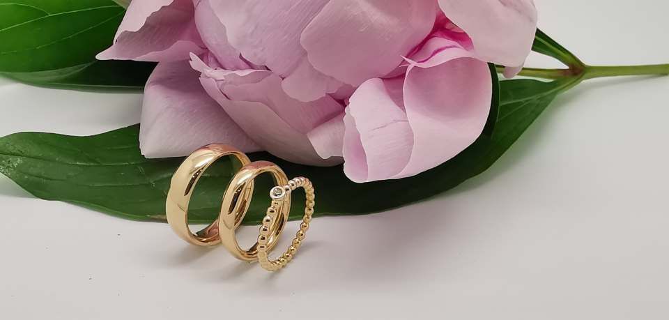 drei goldfarbene Ringe vor einer rosafarbenen Blume