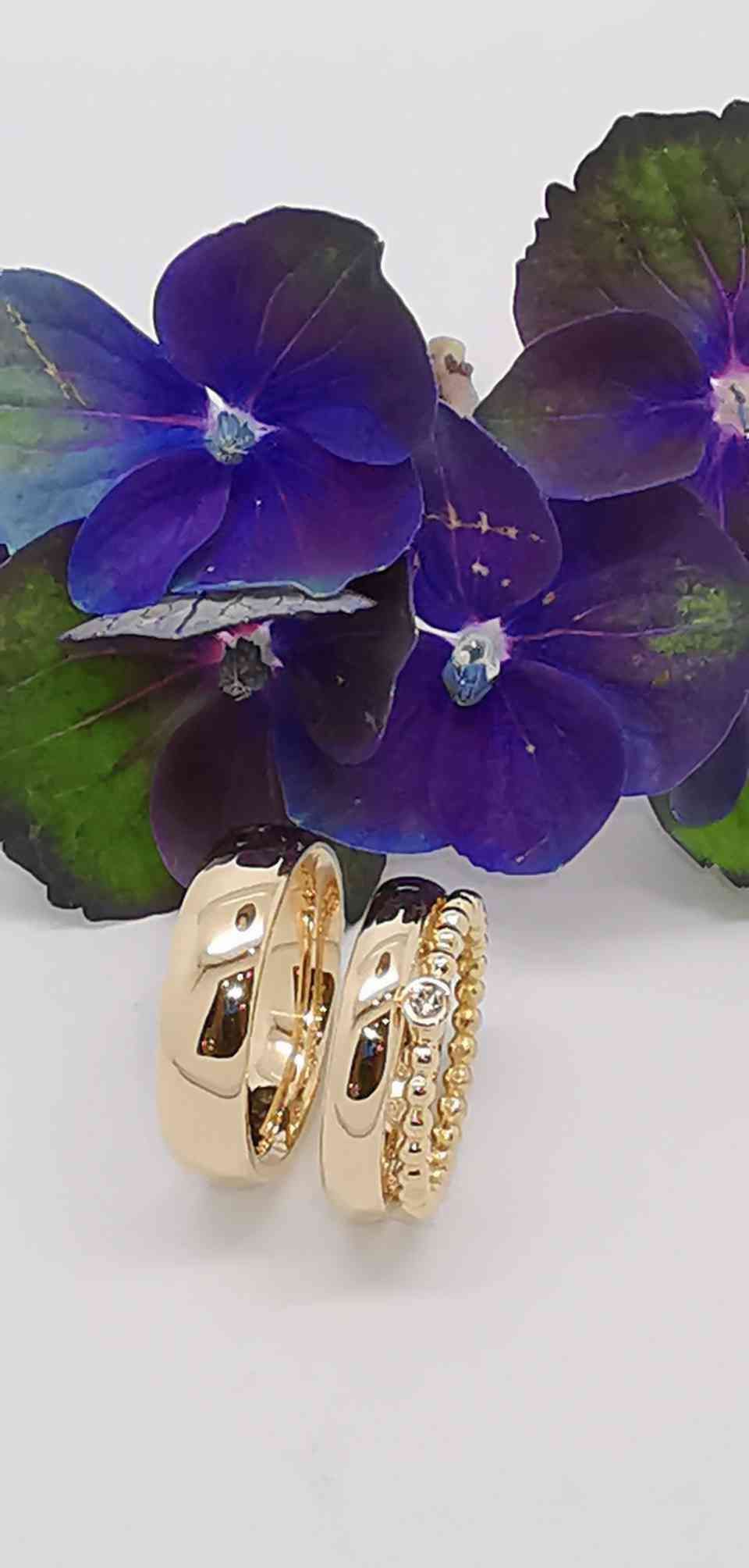 glänzende Trauringe vor einer lilafarbenen Blüte