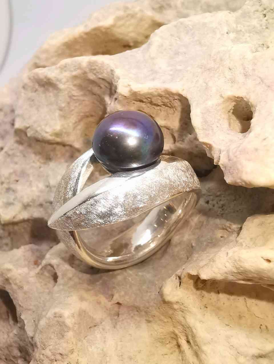 abstrakter Ring mit dunkler Perle auf Steinfläche