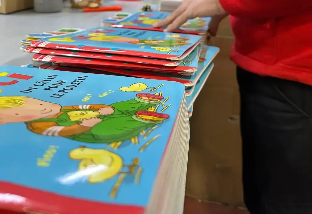 Una persona con una camisa roja está apilando libros sobre una mesa.
