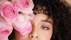Una mujer con cabello rizado sostiene un ramo de rosas rosadas frente a su cara.