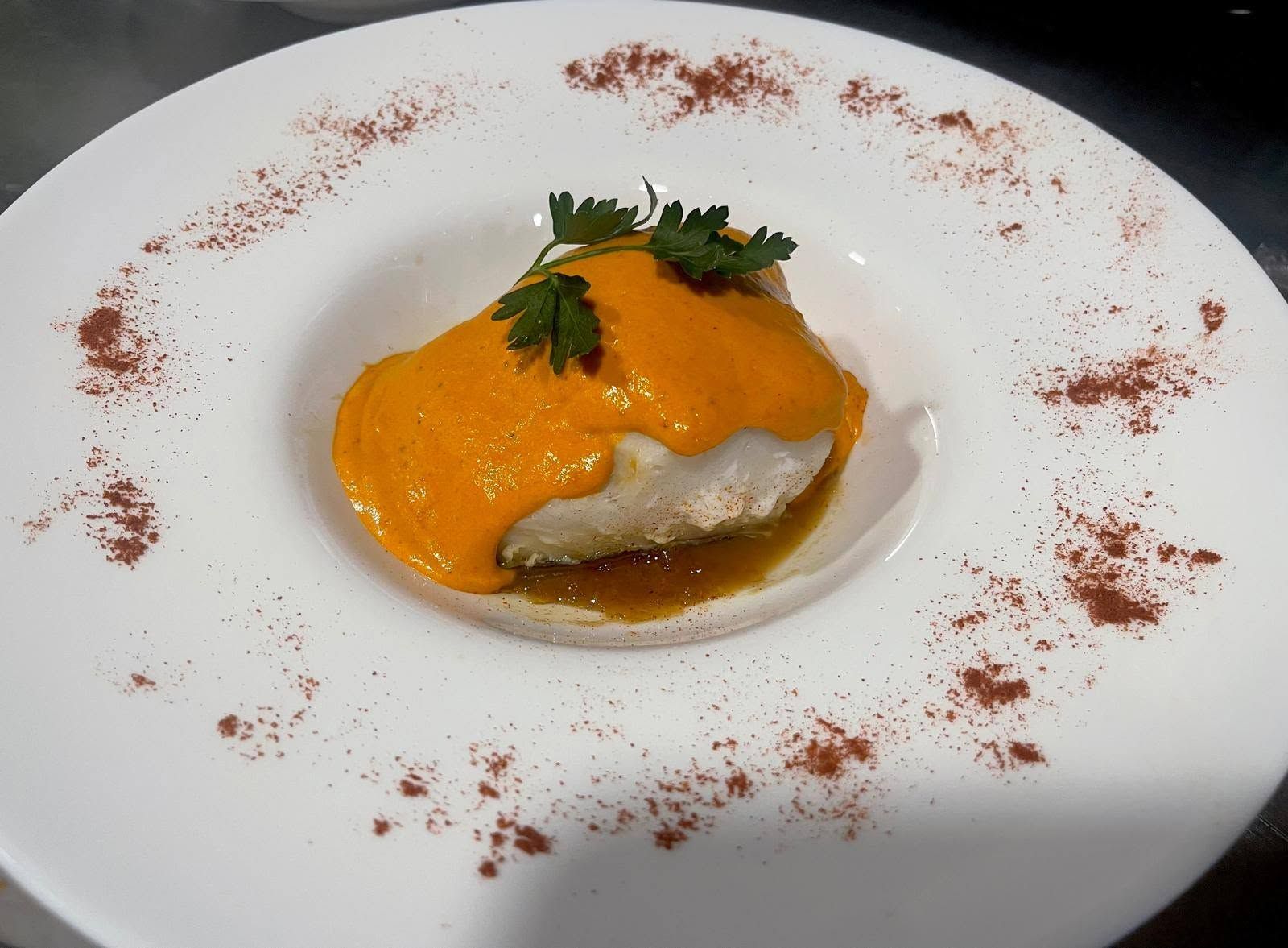 Plato blanco con un filete de pescado cubierto con salsa de naranja, adornado con cilantro y espolvoreado con pimentón