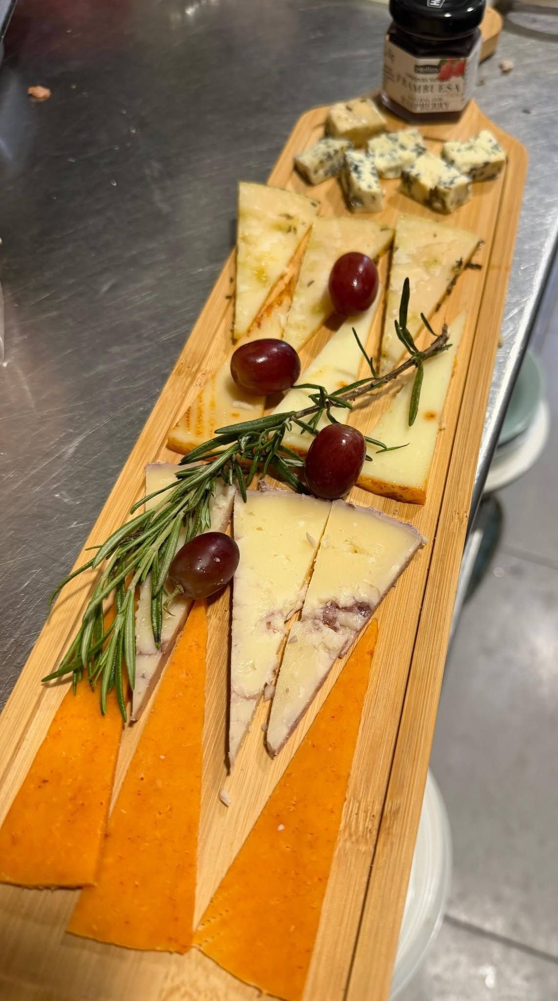 Una tabla de madera para servir con queso en lonchas, uvas, galletas saladas, romero y queso azul de guarnición.