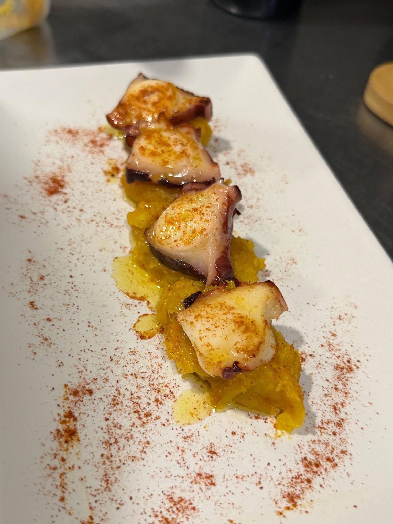 Pulpo a la parrilla en un plato blanco con salsa amarilla y guarnición de pimentón