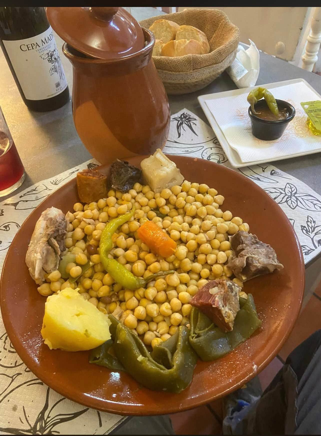 Plato de cuscús con garbanzos, verduras y carne en un plato de terracota junto a una tajine marrón