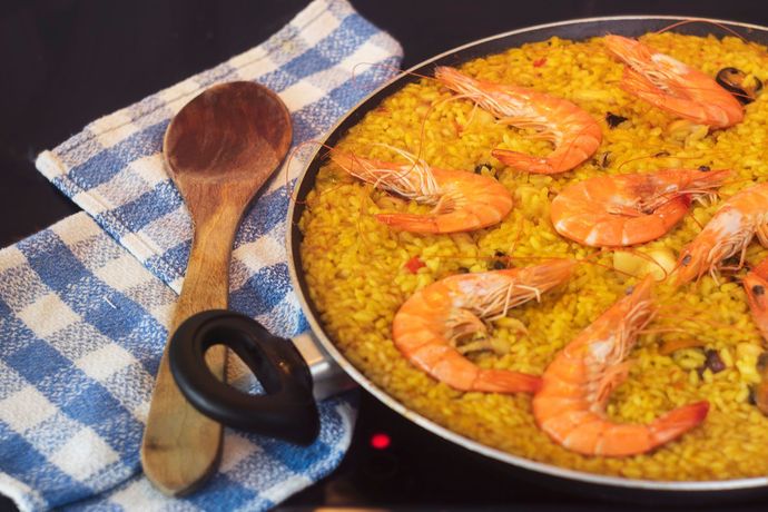 Paella de gambas en una sartén sobre la estufa, junto a una cuchara de madera y un paño de cuadros azules
