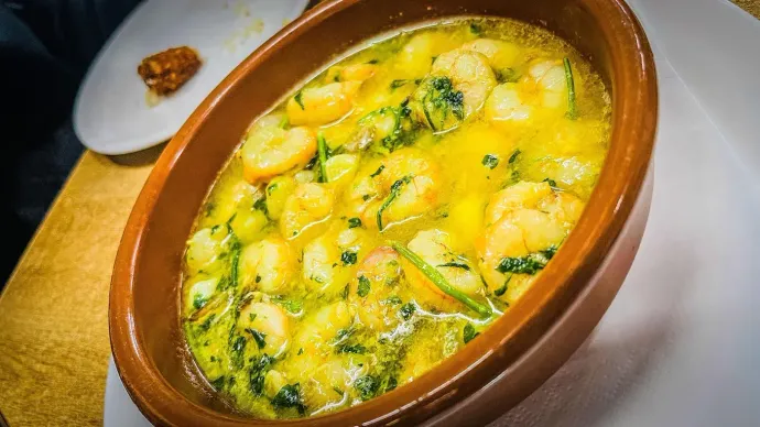 Guiso gratinado con queso, servido en una fuente ovalada marrón y cubierto de queso fundido y hierbas frescas