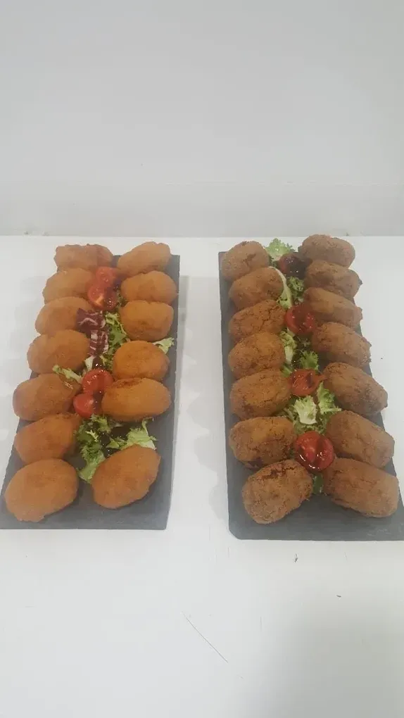 Dos bandejas de aperitivos fritos variados con salsas para mojar sobre una mesa blanca