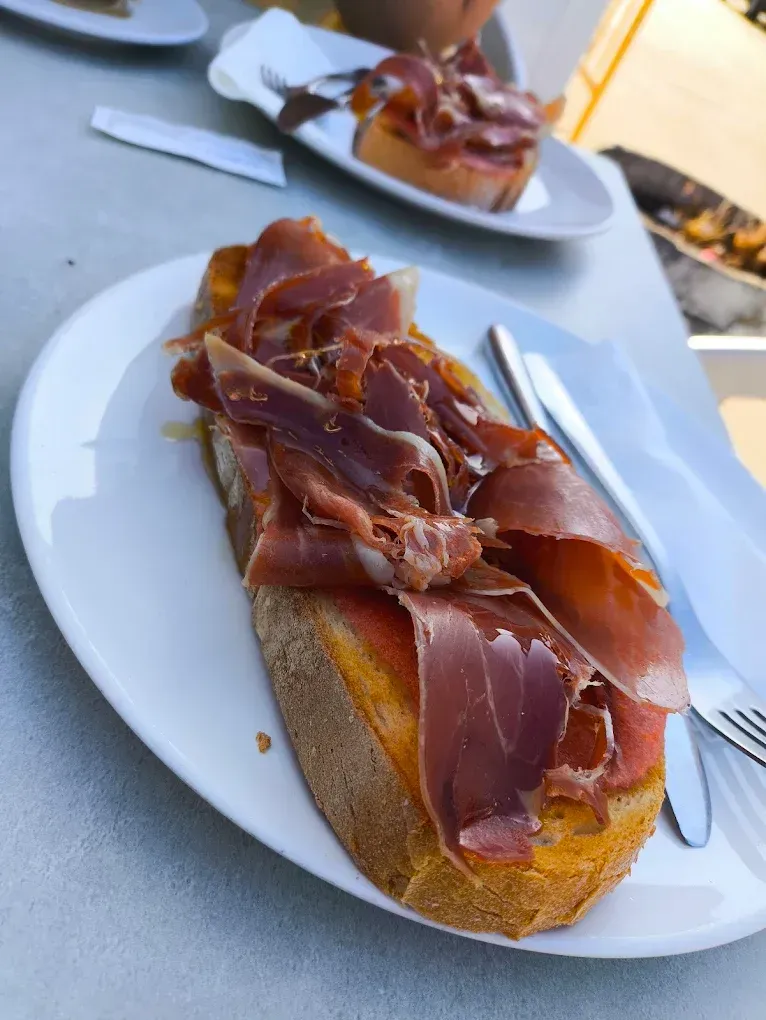 Baguette abierta con jamón, servida en un plato blanco en una cafetería al aire libre