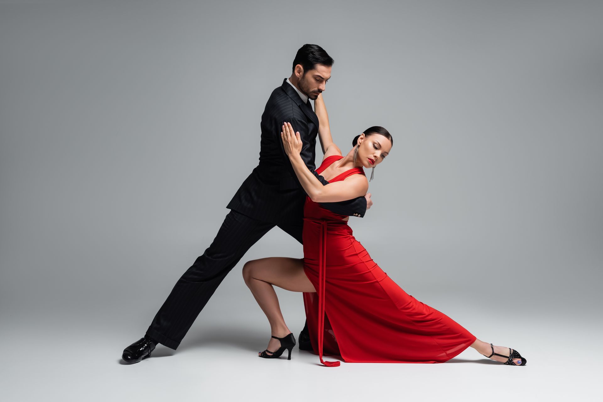 Zwei Personen führen eine dynamische Tango-Figur auf grauem Hintergrund aus