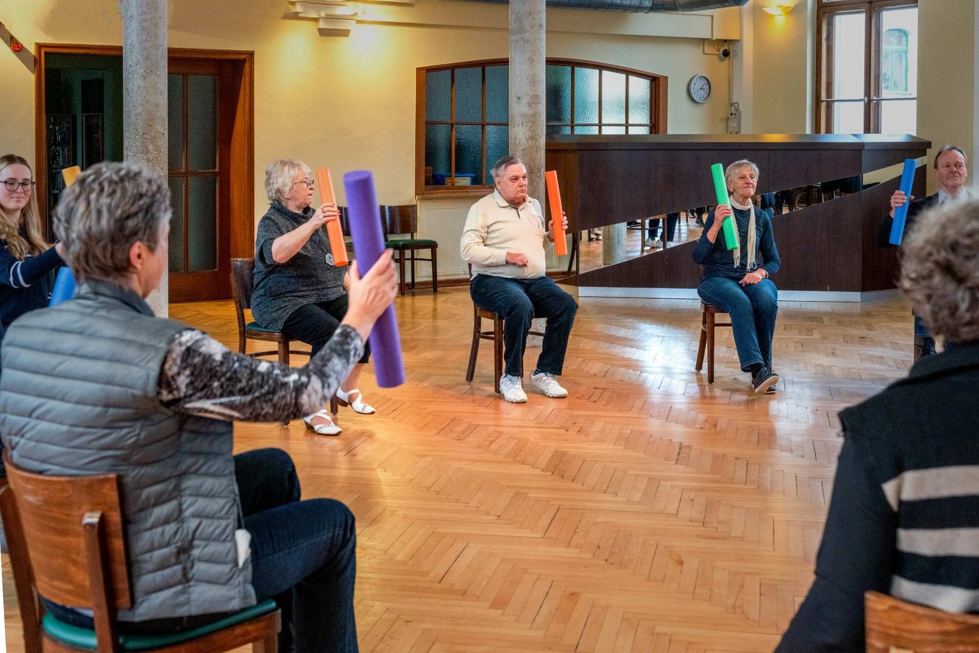 Tanz- oder Bewegungsgruppe in einem großen Raum mit sitzenden und aktiven Teilnehmenden