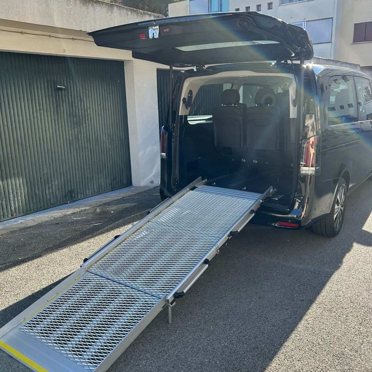 Fourgonnette noire avec hayon arrière ouvert et rampe métallique déployée sur la chaussée.