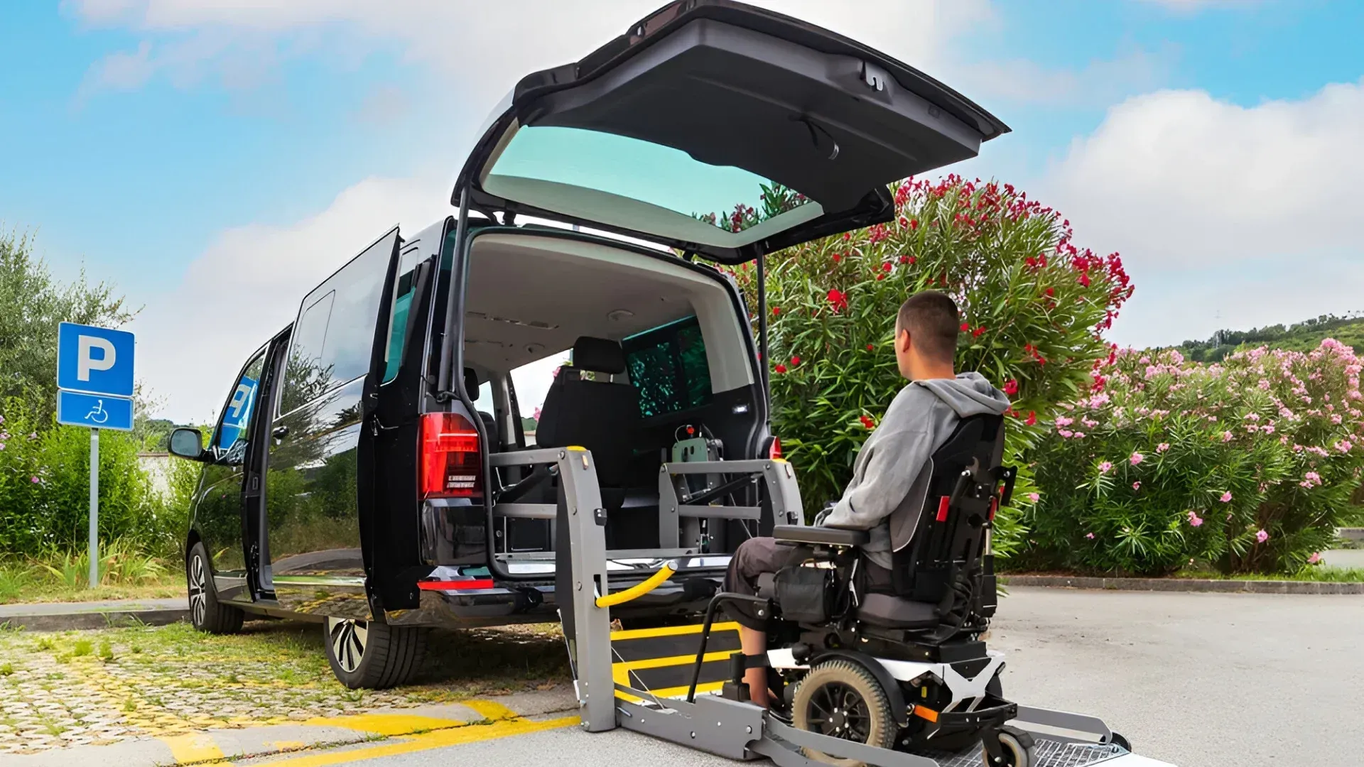 Une personne en fauteuil roulant monte dans une camionnette noire par la rampe d'accès arrière, à l'extérieur près du parking.