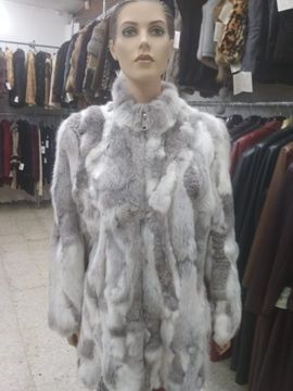 Maniquí con abrigo de piel gris y blanco en una tienda de ropa; otros abrigos visibles al fondo.