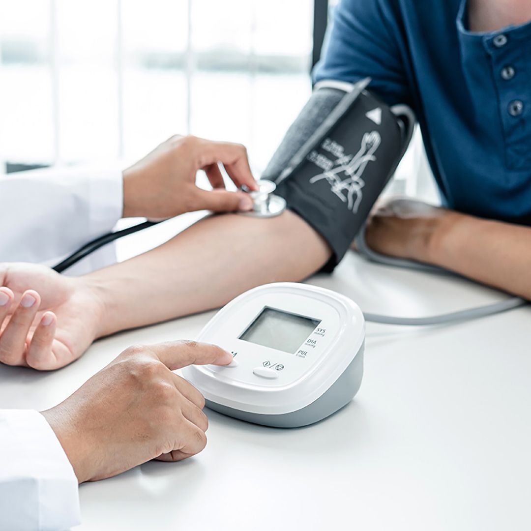Medico che misura la pressione sanguigna del paziente con un bracciale automatico e uno stetoscopio. Tavolo bianco, camicia blu.