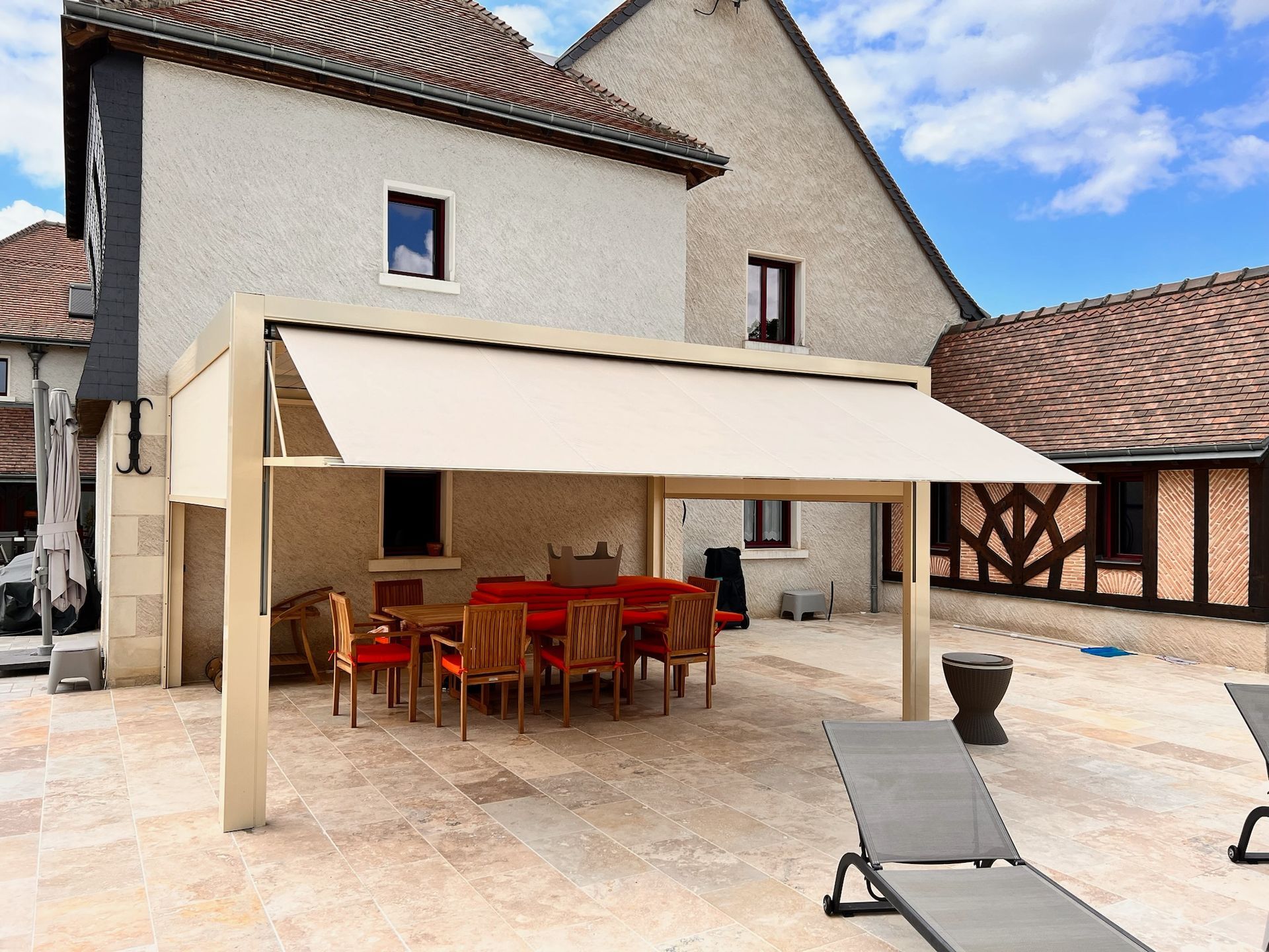 Une pergola beige avec un store recouvre un salon de jardin sur une terrasse en pierre