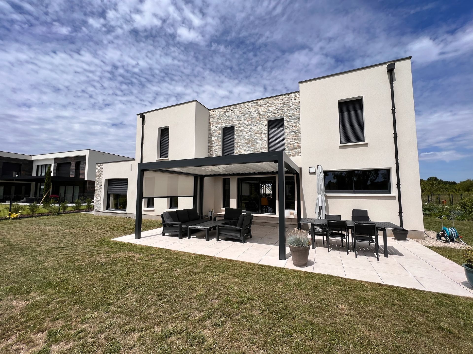 Maison moderne à deux étages avec un coin salon extérieur sous une pergola et une cour gazonnée