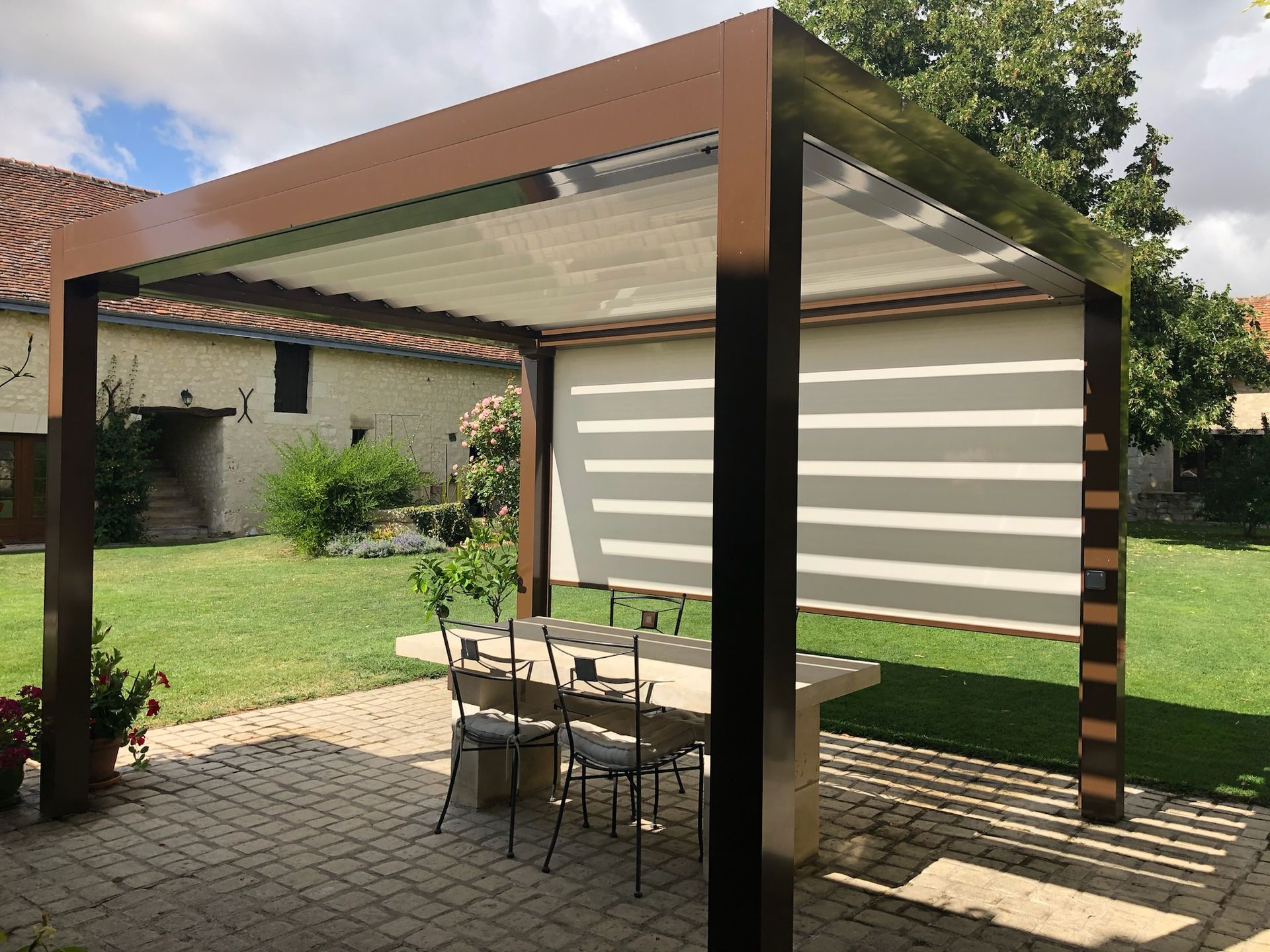 Pergola avec auvent rétractable au-dessus d'une table en pierre et de chaises en fer forgé