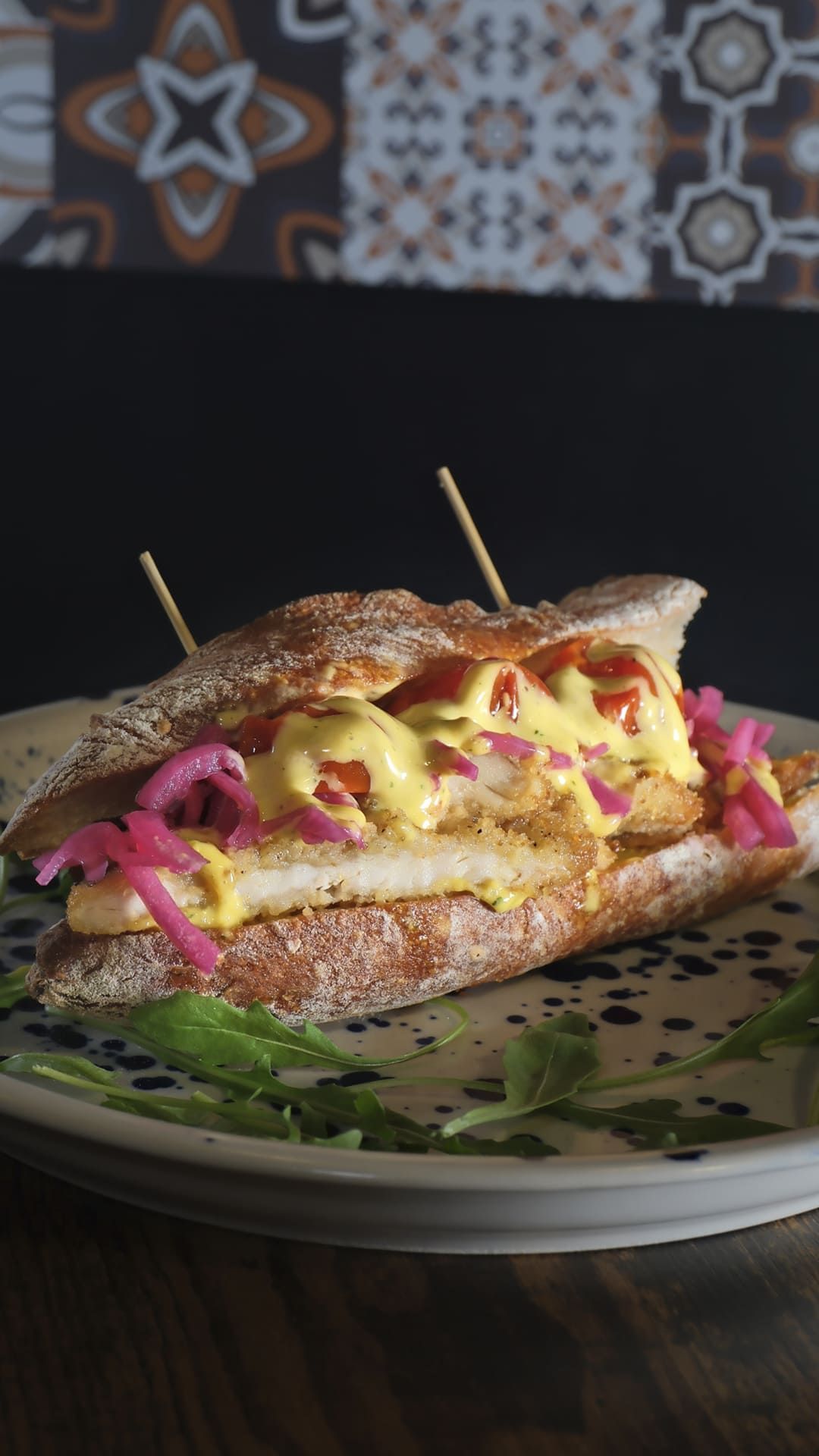 Sándwich a la plancha con queso fundido y cebollas encurtidas, servido en un plato y sujeto con palillos.