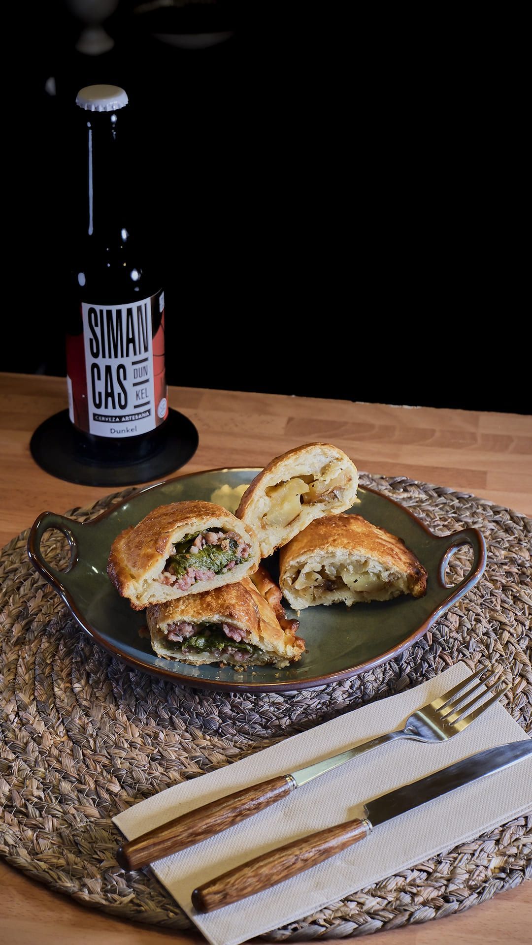 Pasteles salados en un plato con cerveza. Cuchillo y tenedor sobre un mantel individual tejido.
