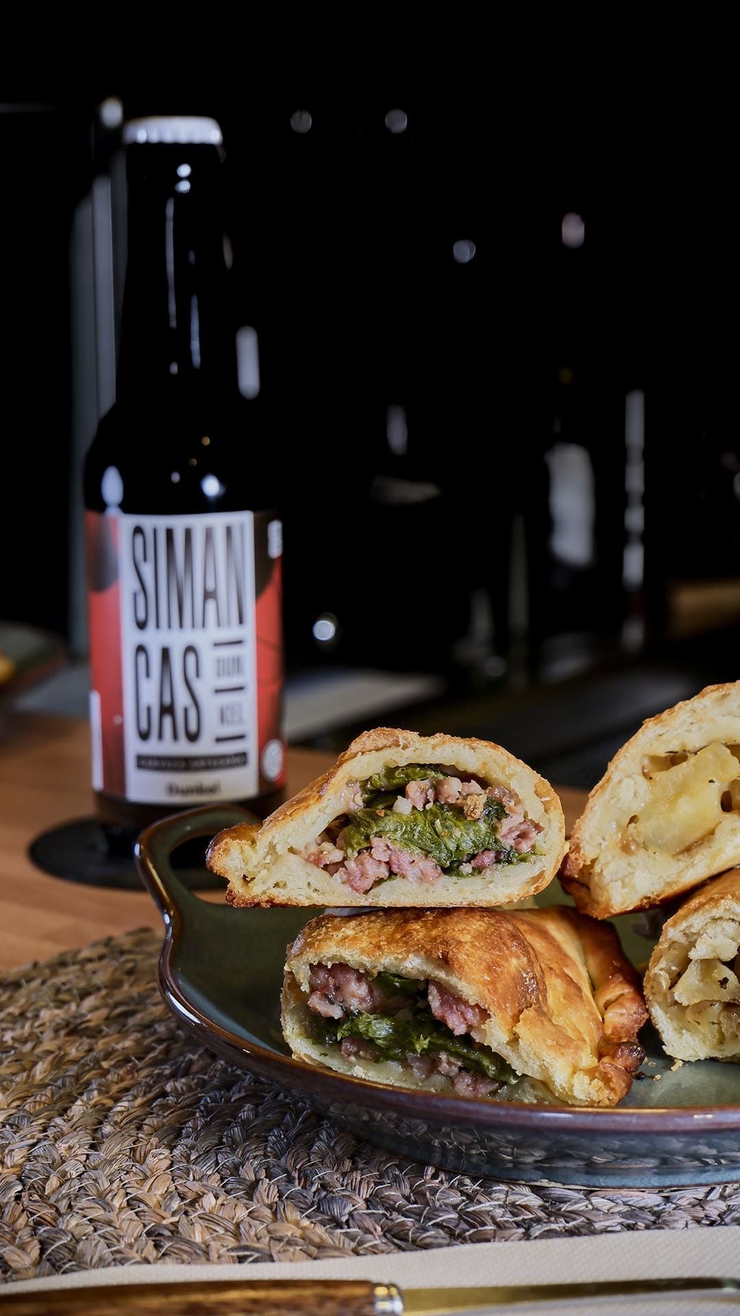 Pasteles salados en un plato, junto a una botella de cerveza negra. Primer plano de la comida y la bebida.