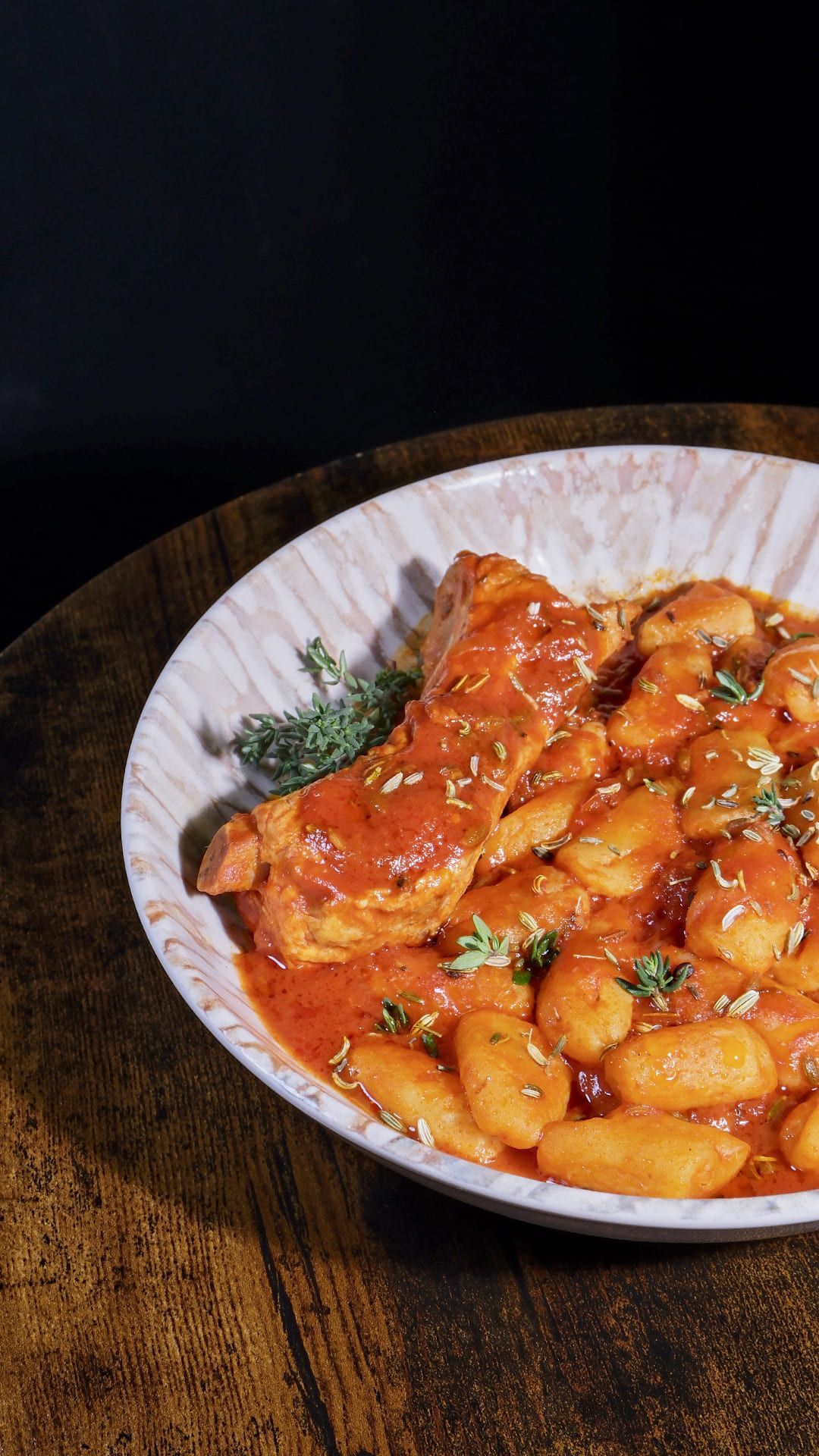 Primer plano de un bol de ñoquis y una chuleta rebozada en salsa de tomate, espolvoreada con semillas de sésamo, sobre una mesa de madera.
