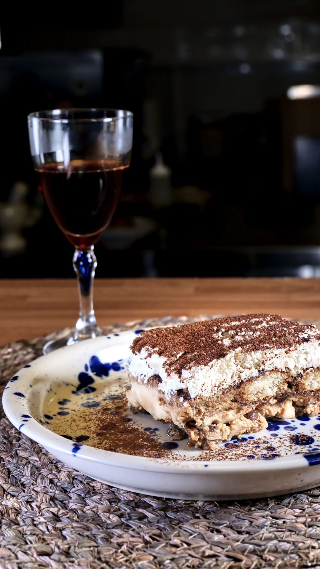 Postre de tiramisú servido en un plato con una copa de vino tinto. Cacao en polvo espolvoreado.