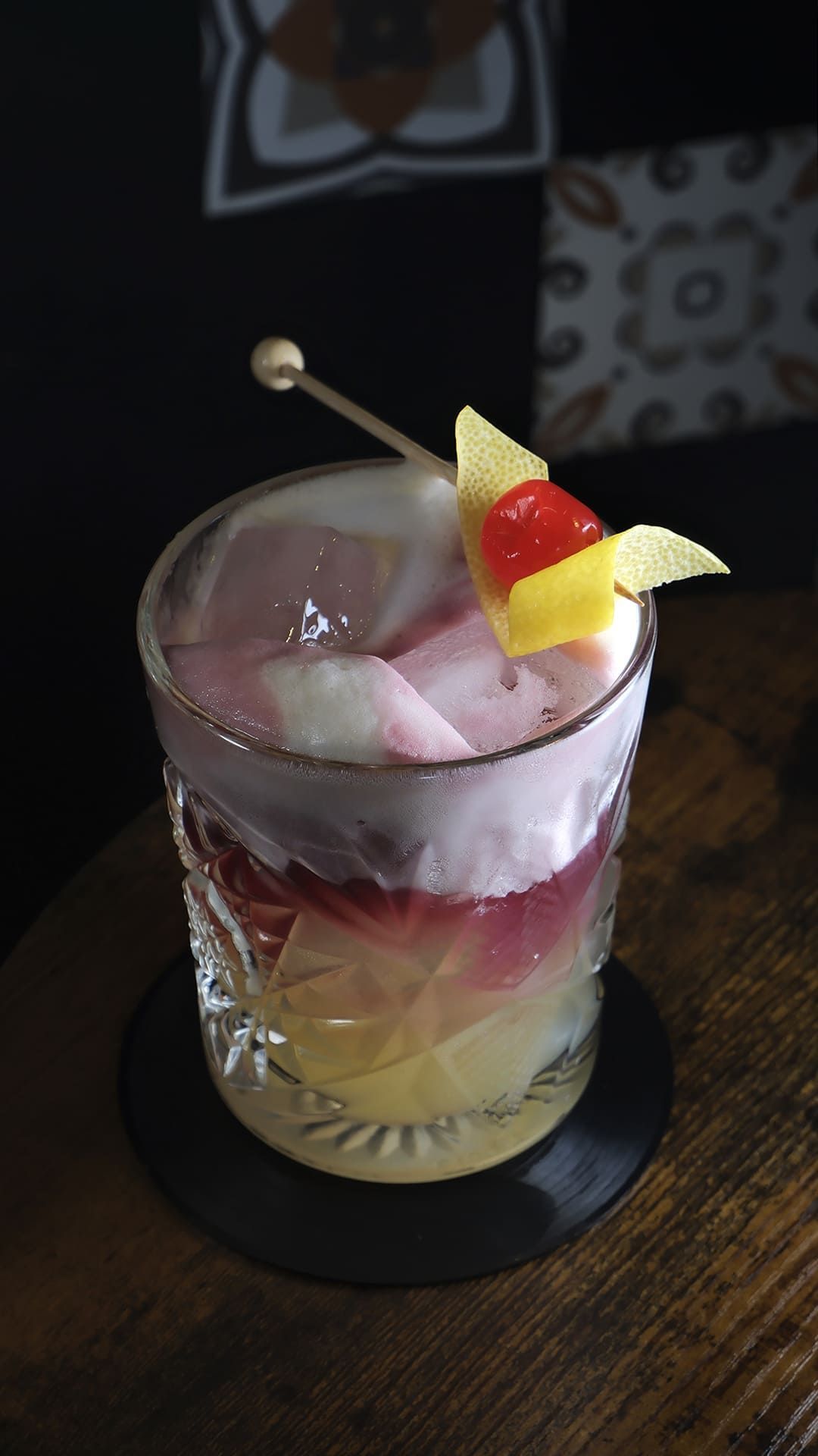 Cóctel servido en un vaso bajo con hielo y guarnición de fruta sobre una mesa de madera.