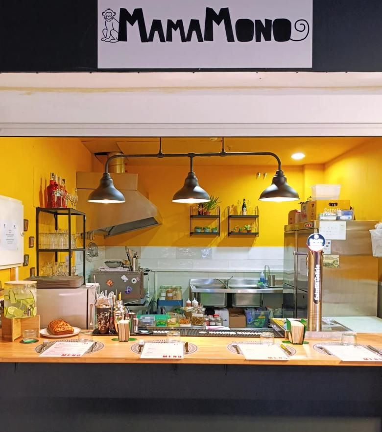 Interior de restaurante con una pared amarilla y blanca detrás de un mostrador de madera; cartel de MamaMono.