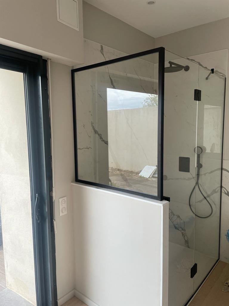 Cabine de douche moderne avec parois en verre et finitions noires ; murs blancs et carrelage en marbre.