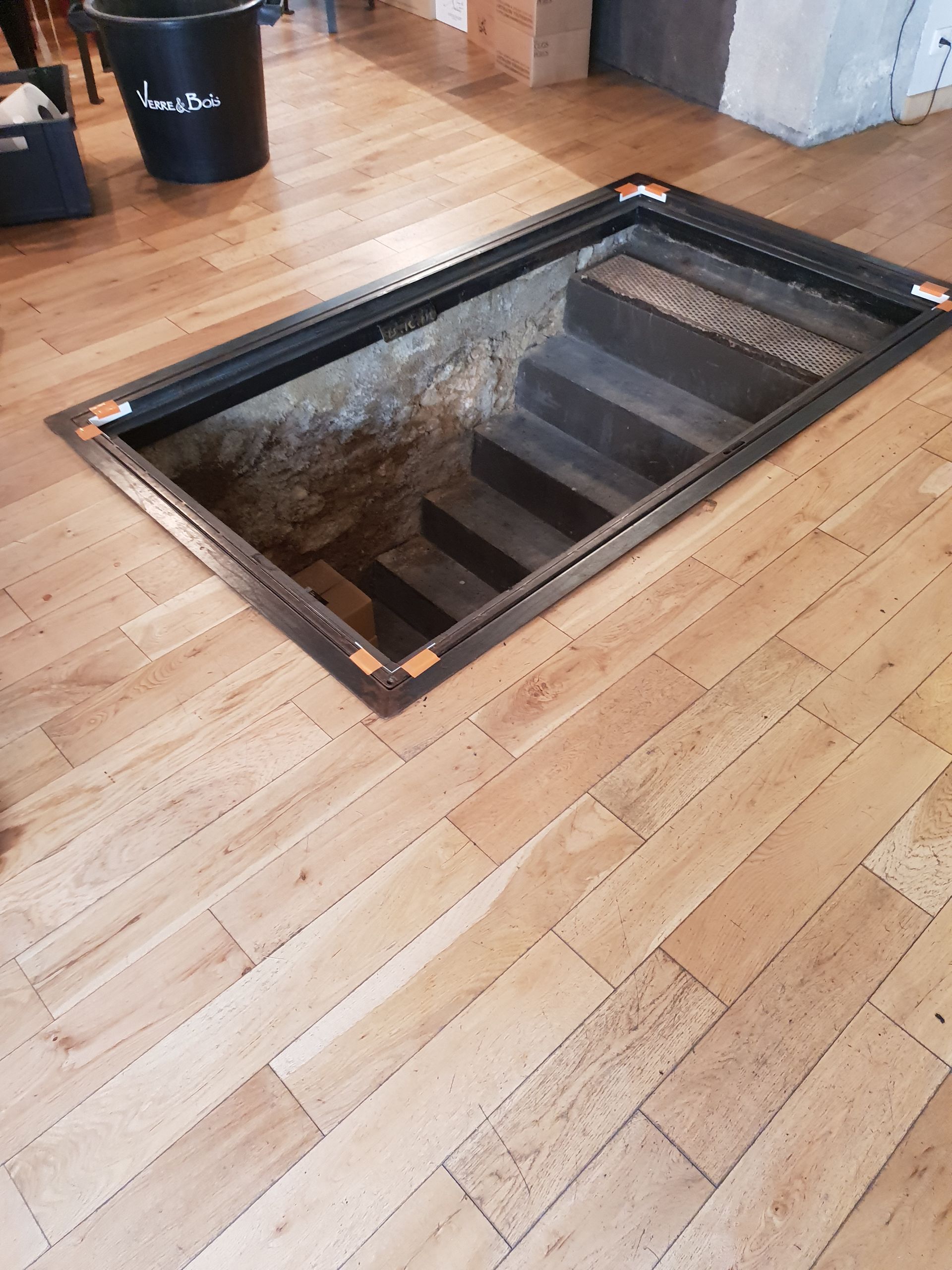 Sol en bois avec un escalier encastré descendant, encadré de noir.