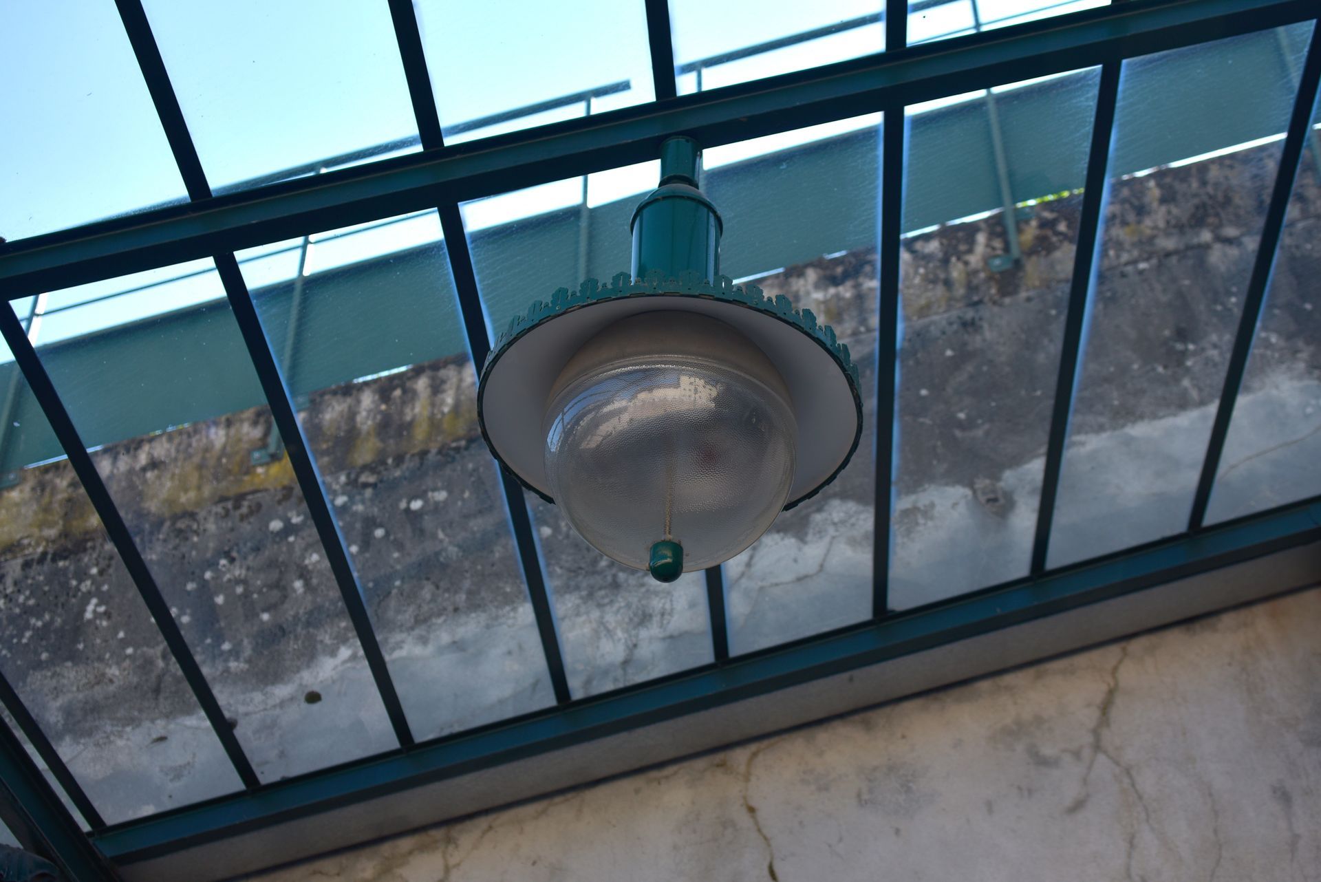 Plafond en verre à cadre vert avec une lampe sphérique suspendue. Mur en béton en arrière-plan.