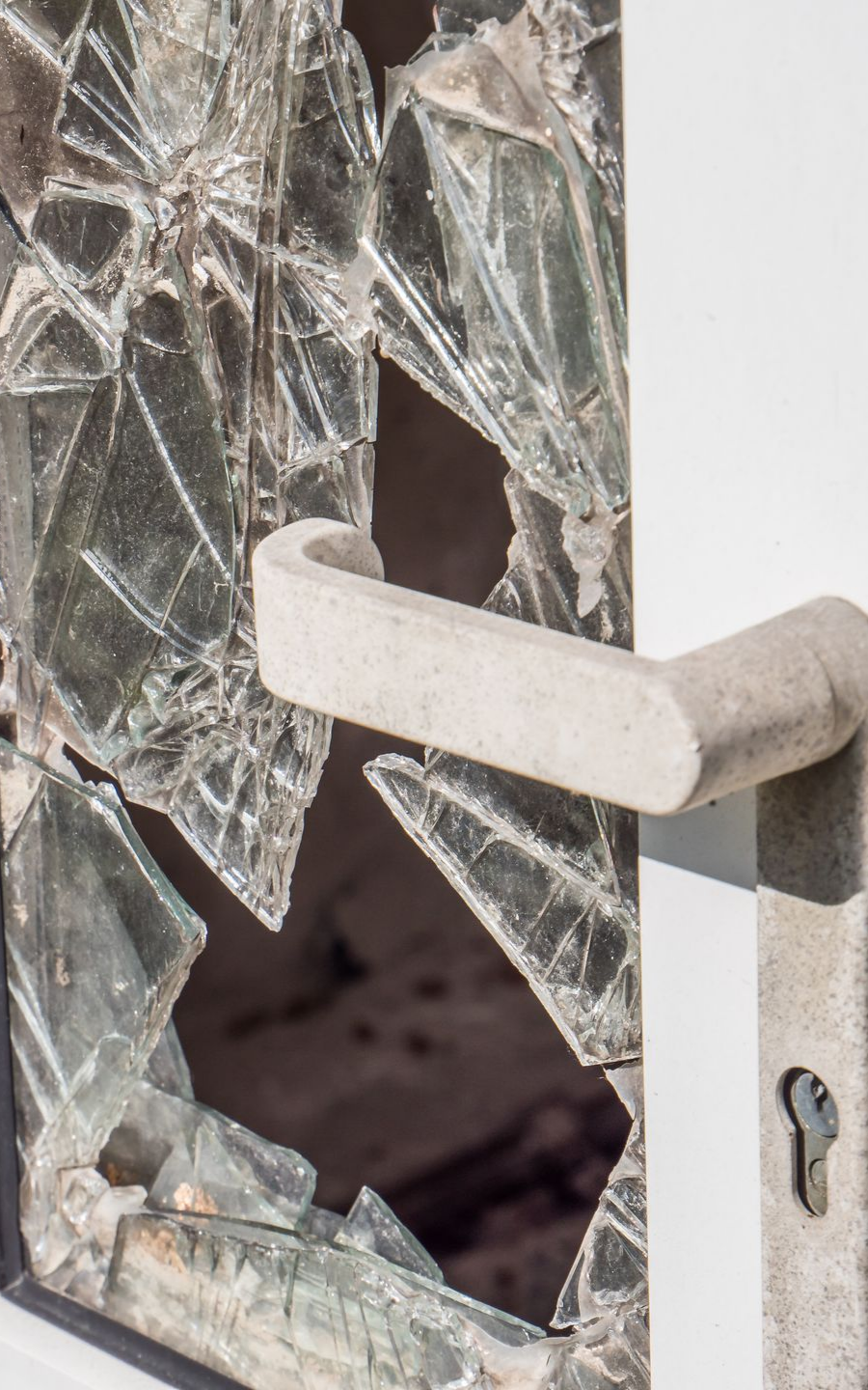 Vitre brisée d'une porte blanche avec une poignée de porte en béton.