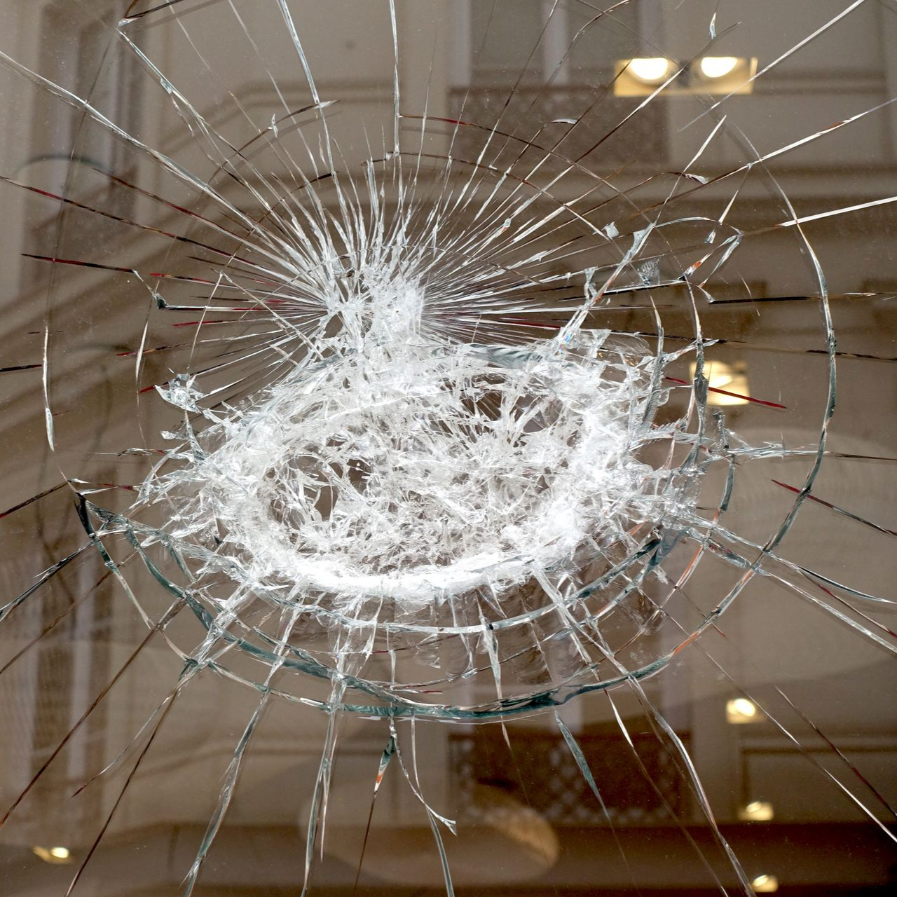 Vitre brisée présentant un point d'impact circulaire. Reflets des bâtiments extérieurs dans le verre.