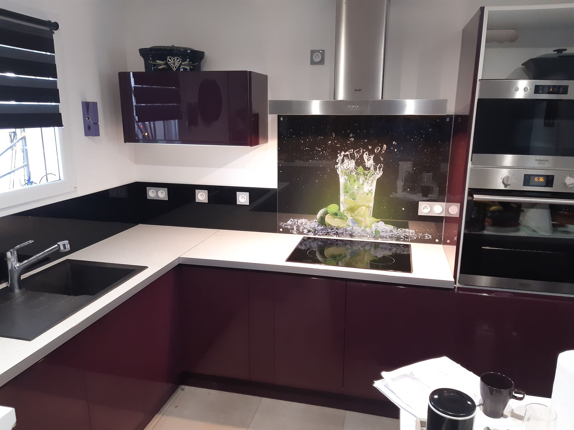 Cuisine moderne avec des armoires violet foncé, des comptoirs clairs et une crédence en verre à motif floral.