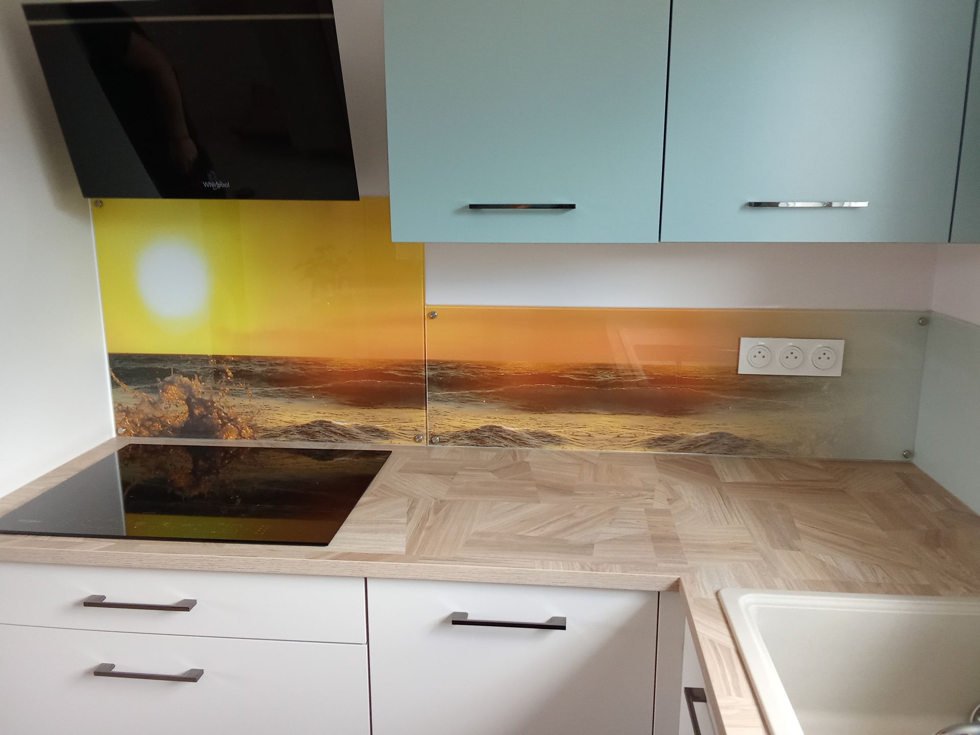 Cuisine avec crédence à motif de plage, placards bleu clair, comptoirs et placards blancs.